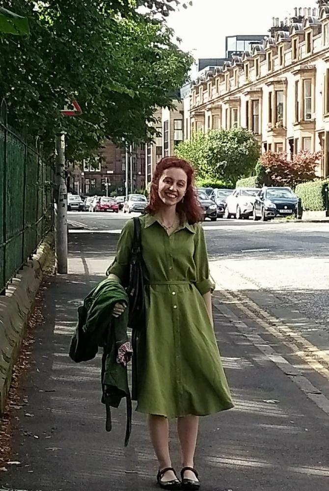 A person in a green dress standing in a street with terraced houses in the background