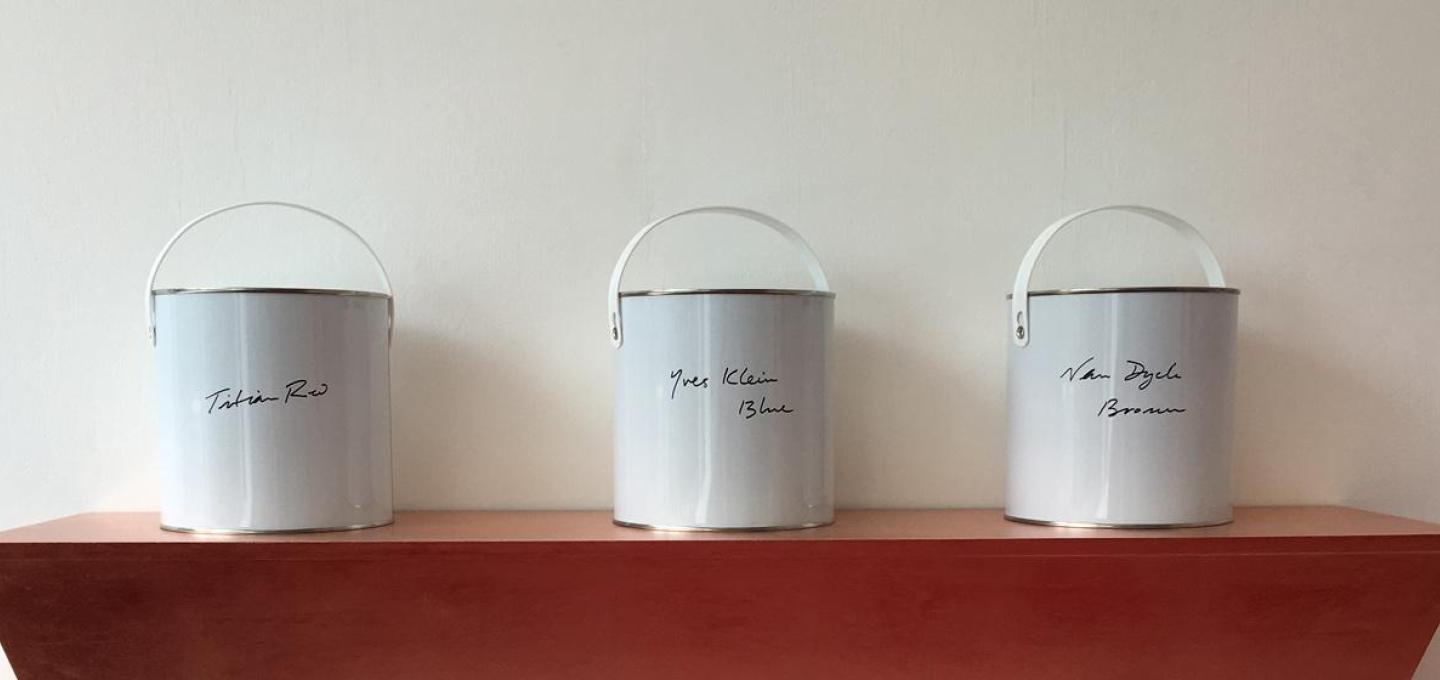 Three white paint tins on a brown shelf. Each tin has different text handwritten on them