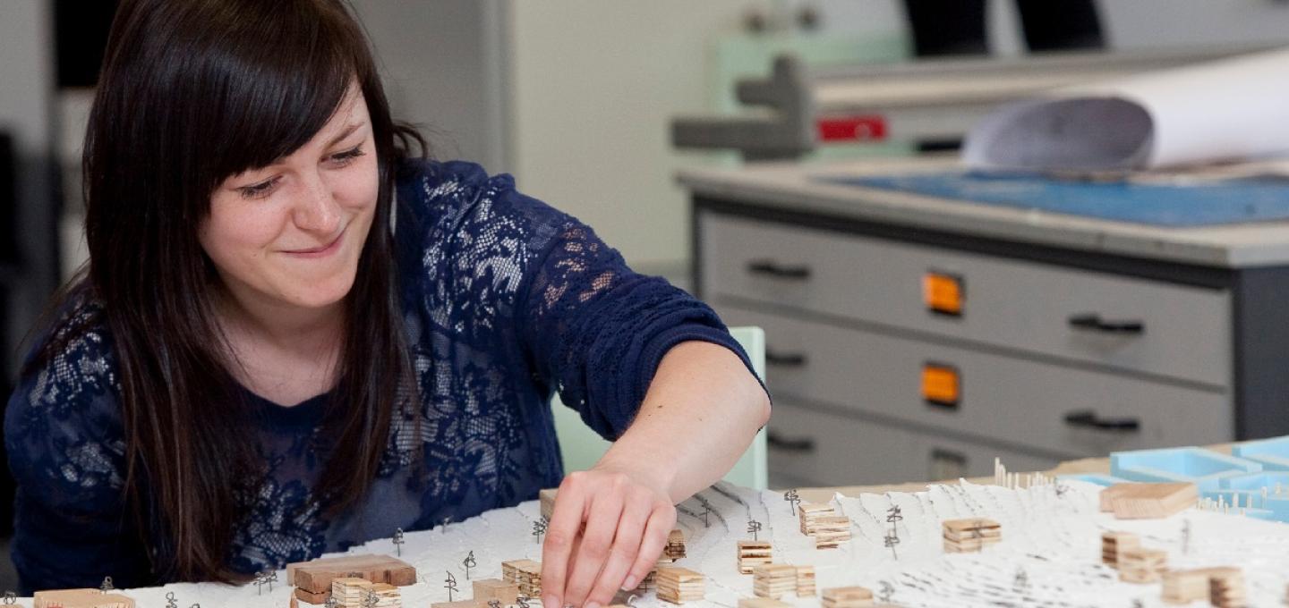 A student works contructing an architectural model on a desk