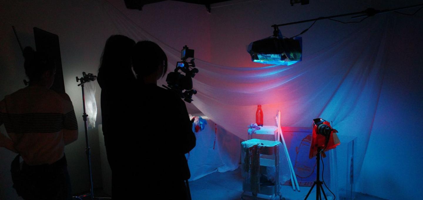Wide shot of camera crew filming in a studio with dim neon lights