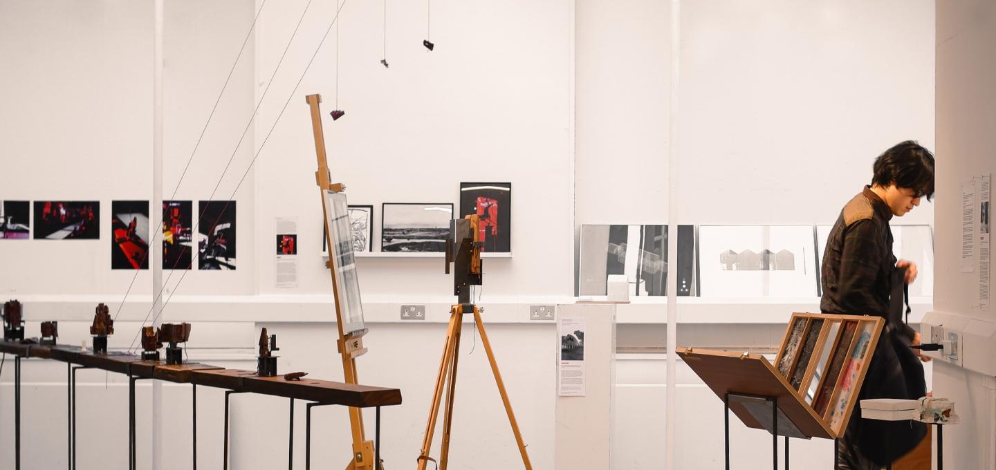 A student reading material in an exhibition, containing models, installations, drawings and photographic prints.