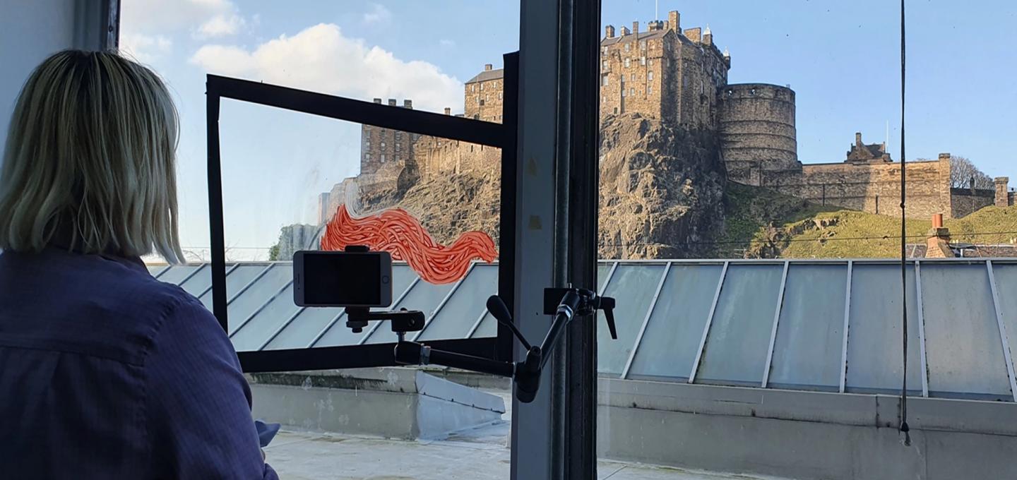 female student with a camera and painted glass looking out of the window at Edinburgh Castle