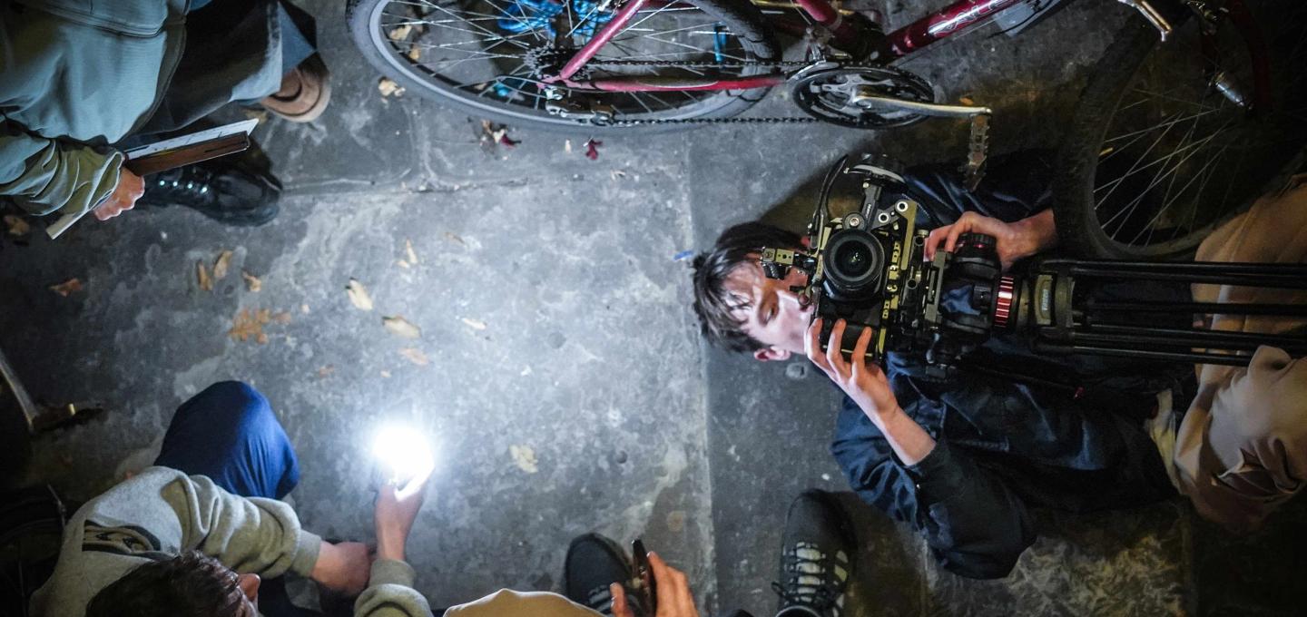 a bird's eye view shot of a person lying on their back holding a camera upwards, with other people around them and a bicycle in shot