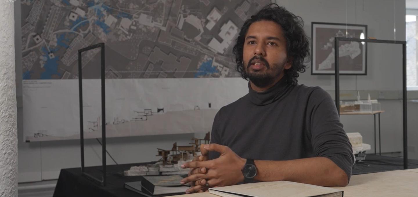 A student on the Architectural and Urban Design programme sits in one of the studios, surrounded by student work.