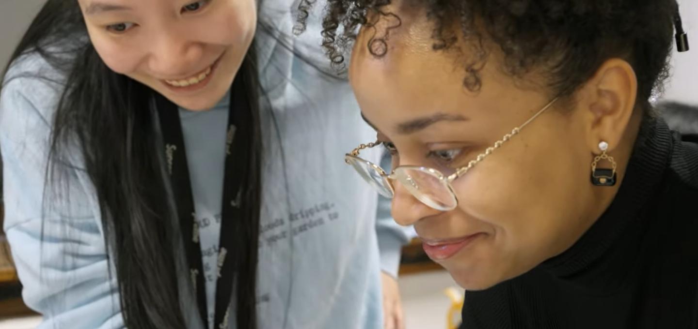 Two students look at a laptop in a studio space.
