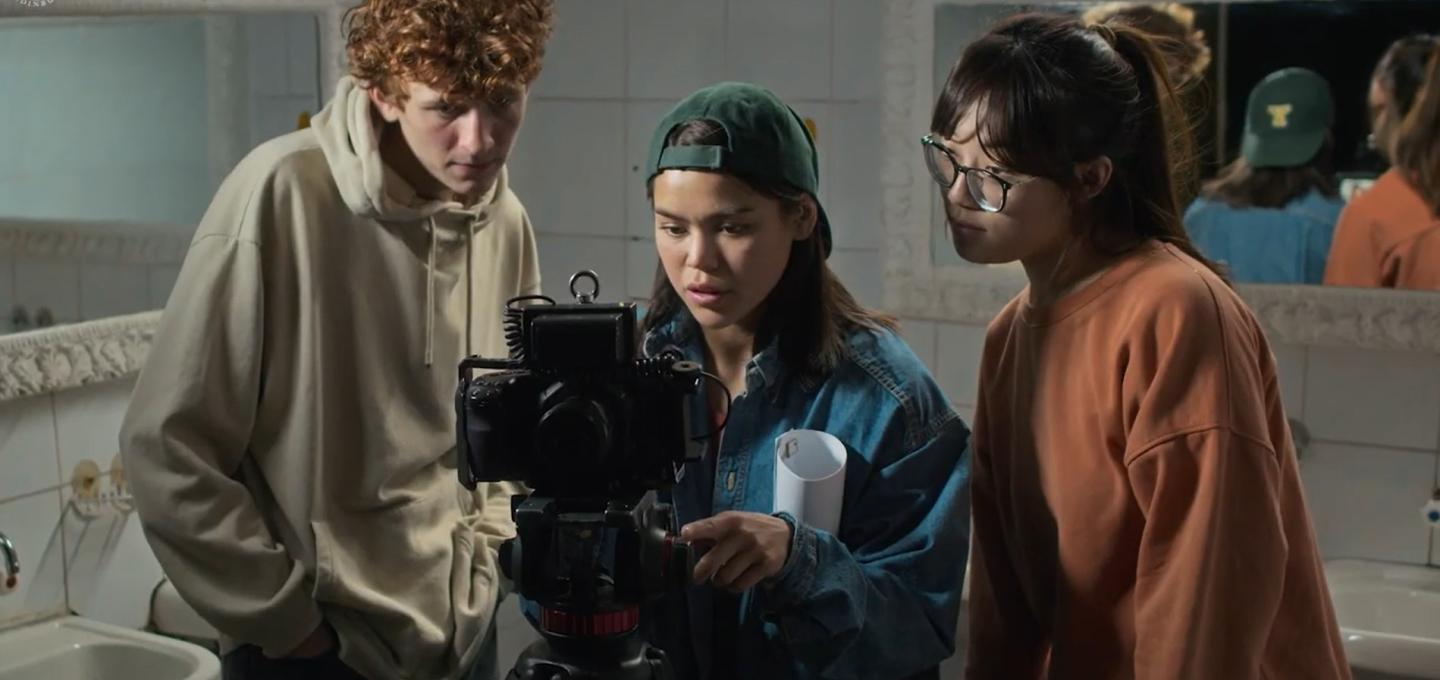 Three students on the Film Art MA programme stand around a camera on the set of their film.