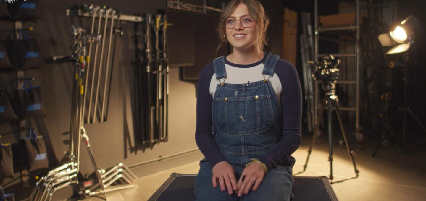 A student on the Film Directing MA programme sits in a film studio, surrounded by lighting and film equipment.