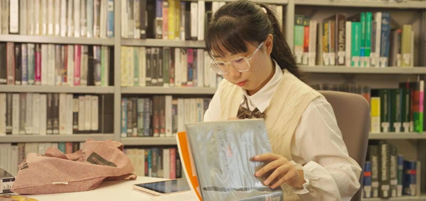 A student on the History, Theory and Display programme sits in the library with a book called Art and Artists.