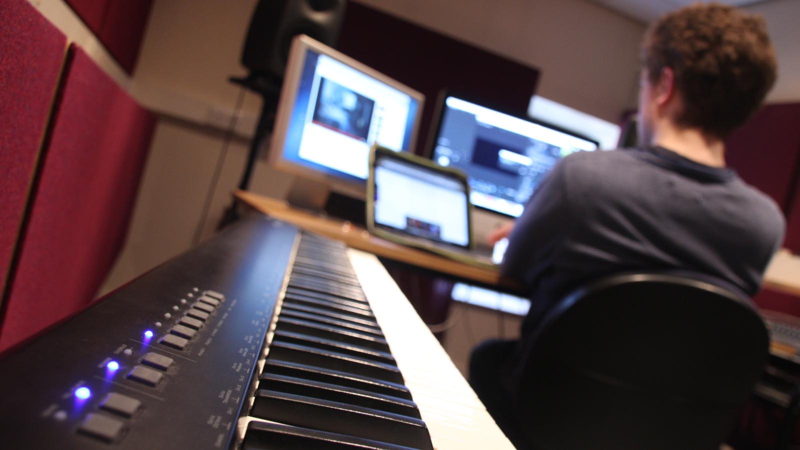 Student working at computer in the background with a close-up of a piano keyboard in the foreground