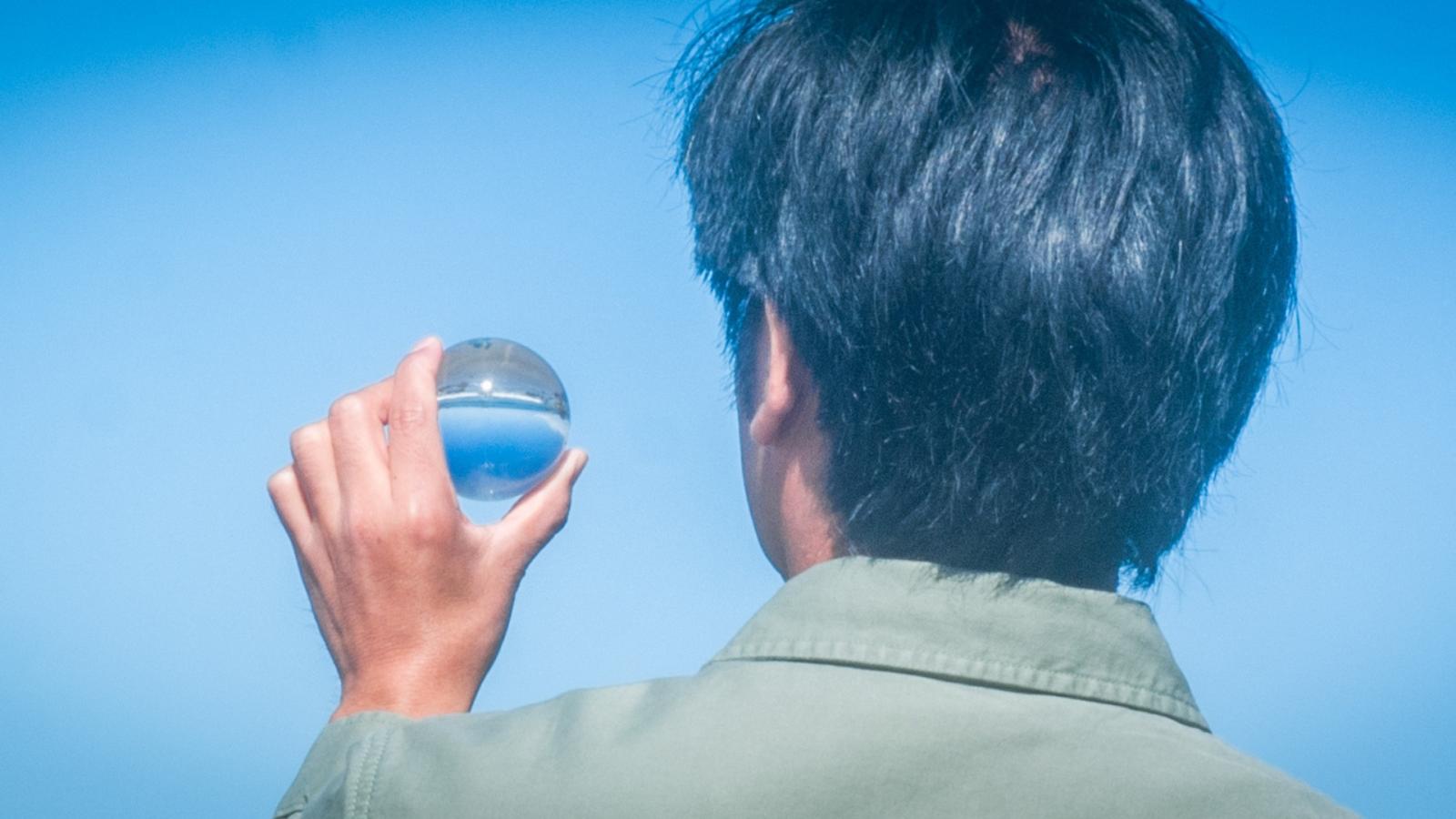 The back of someone's head as they look at a small glass ball they are holding