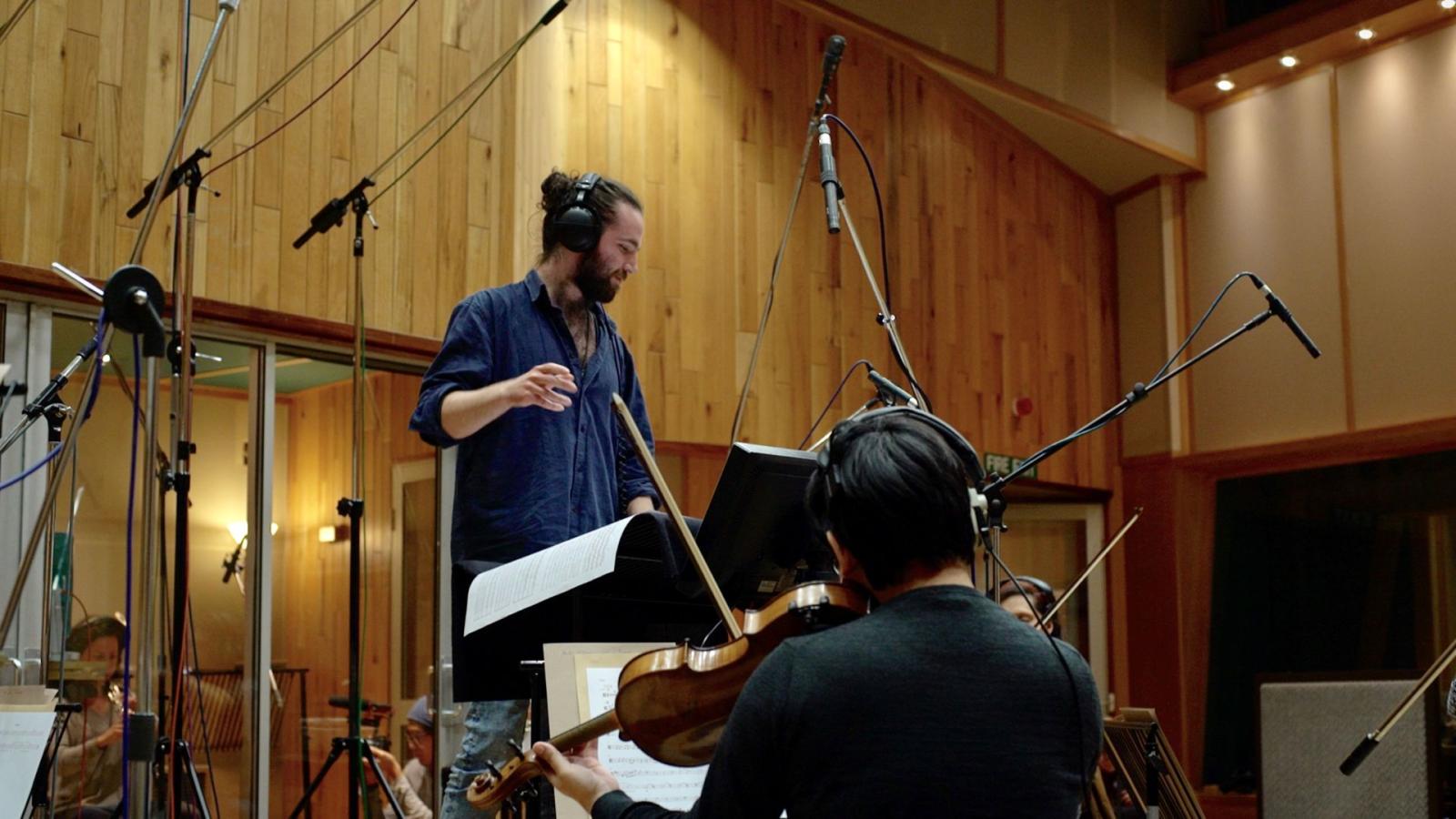 A photo of Joseph in a recording studio conducting a group of musicians out of shot.