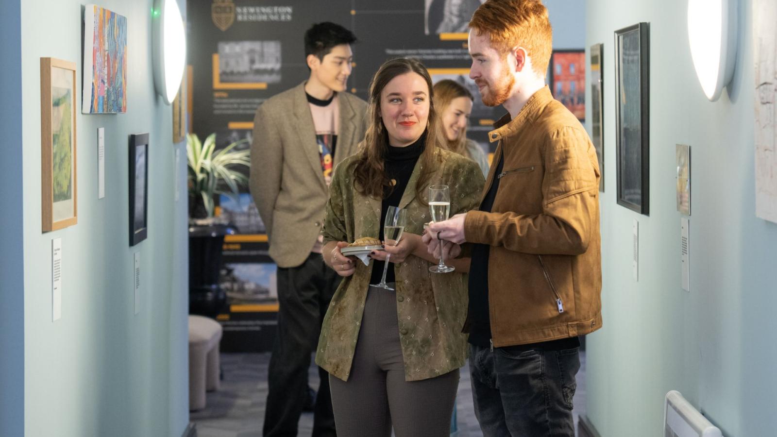 Two students viewing artwork on display on a wall.