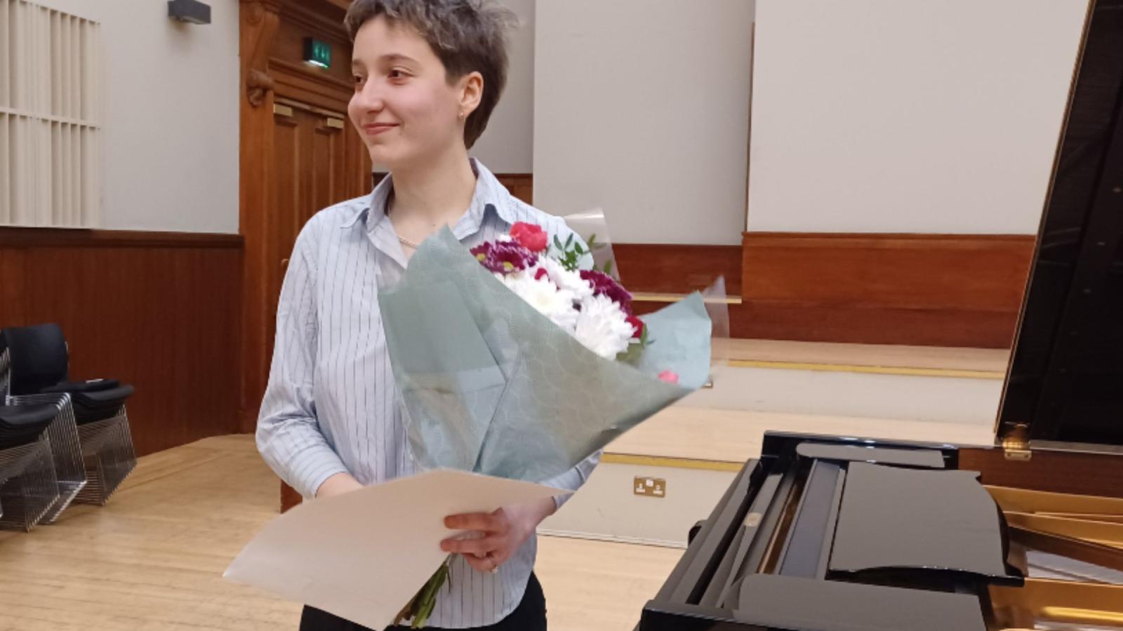 A photo of first prize winner Paloma holding a bouquet of flowers at a piano