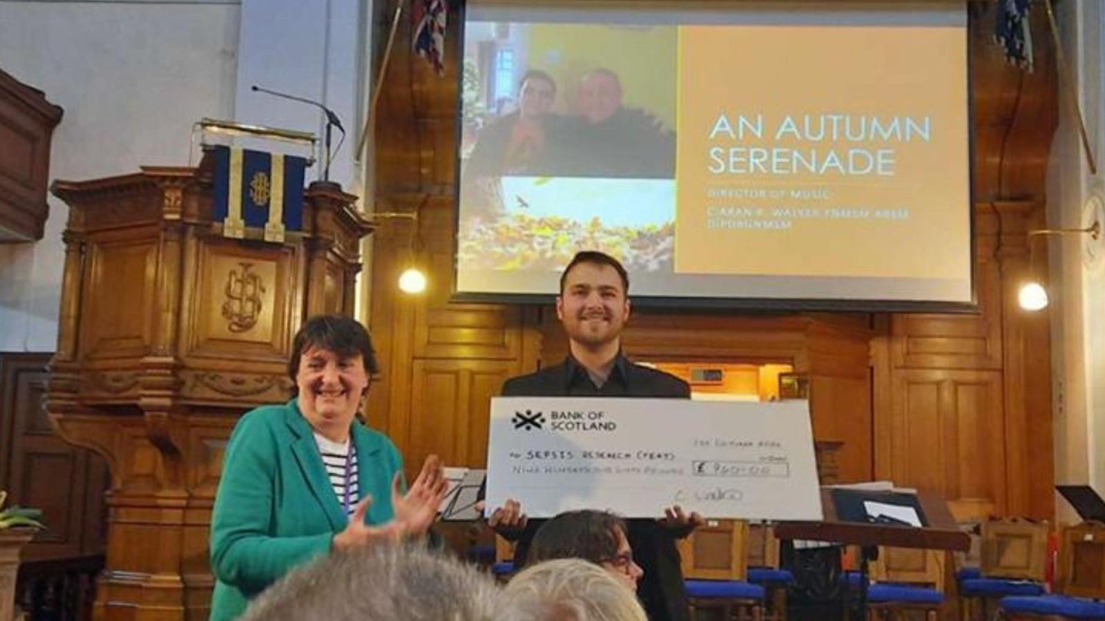 Two people presenting a large charity cheque in a church hall
