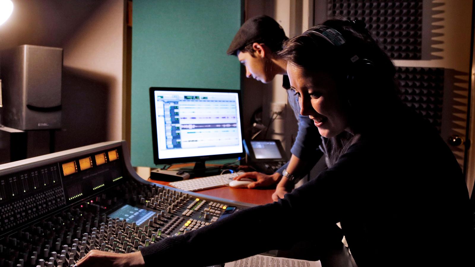 Two music students working on mixers and computers in a recording room.