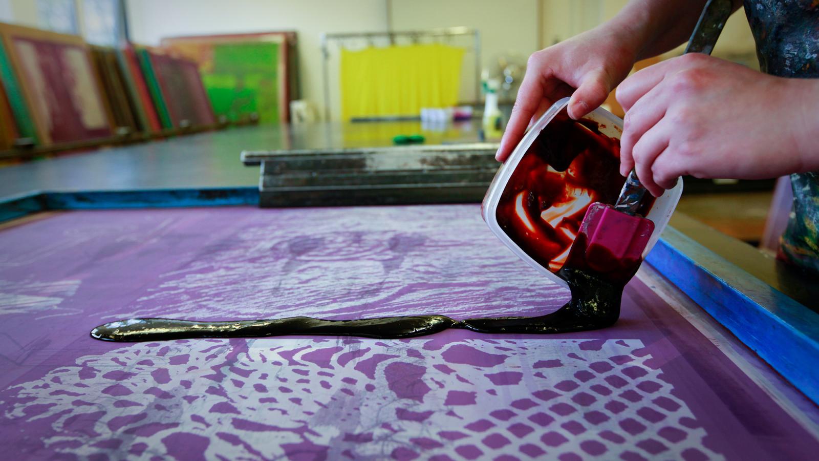 A student pours thick printing ink onto a printing screen.
