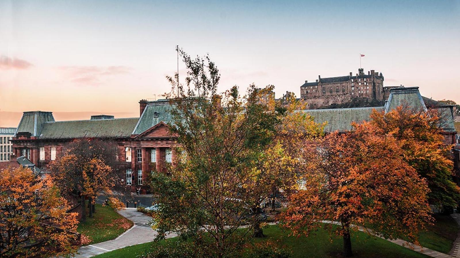 The ECA Main Building pictured at sunset on an autumn evening. Edinburgh Castle is in the background.