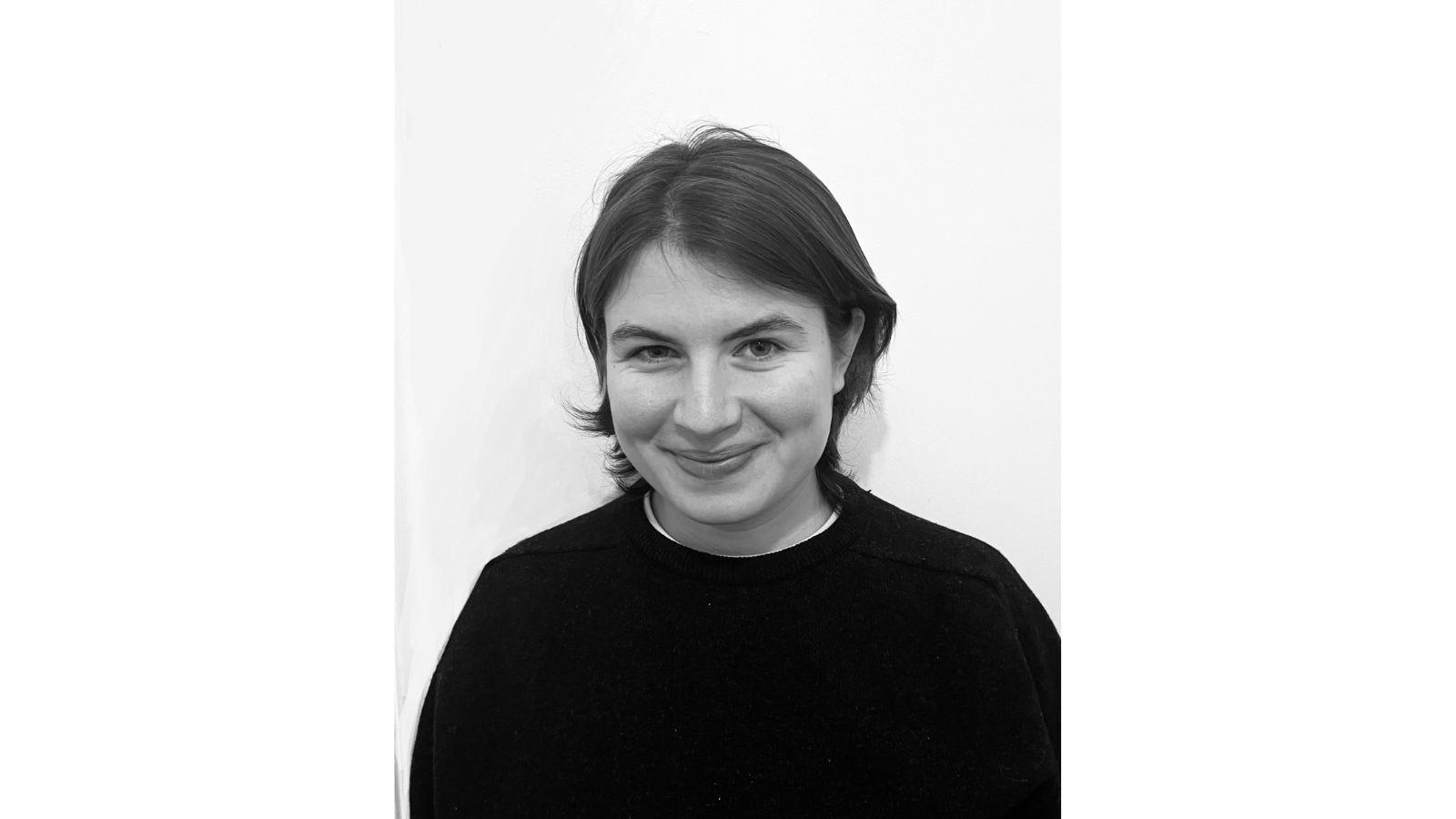 A head and shoulders photograph of Prune. She's wearing a black top, has dark hair cut just above the shoulder, and is smiling at the camera