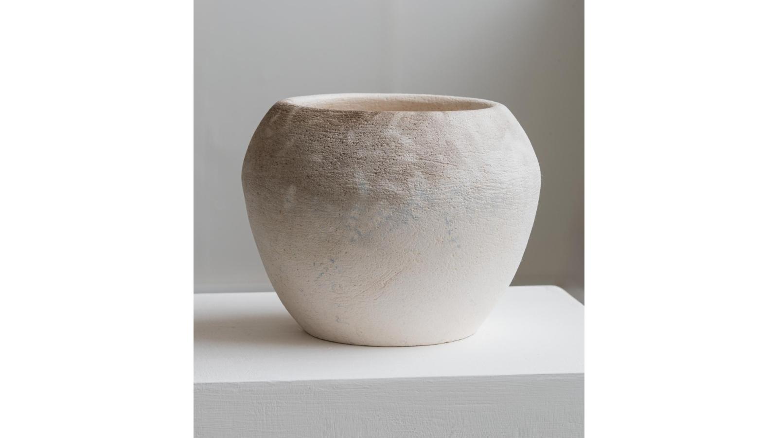 A circular pot. It is is white, with some shading and patterns towards the top.