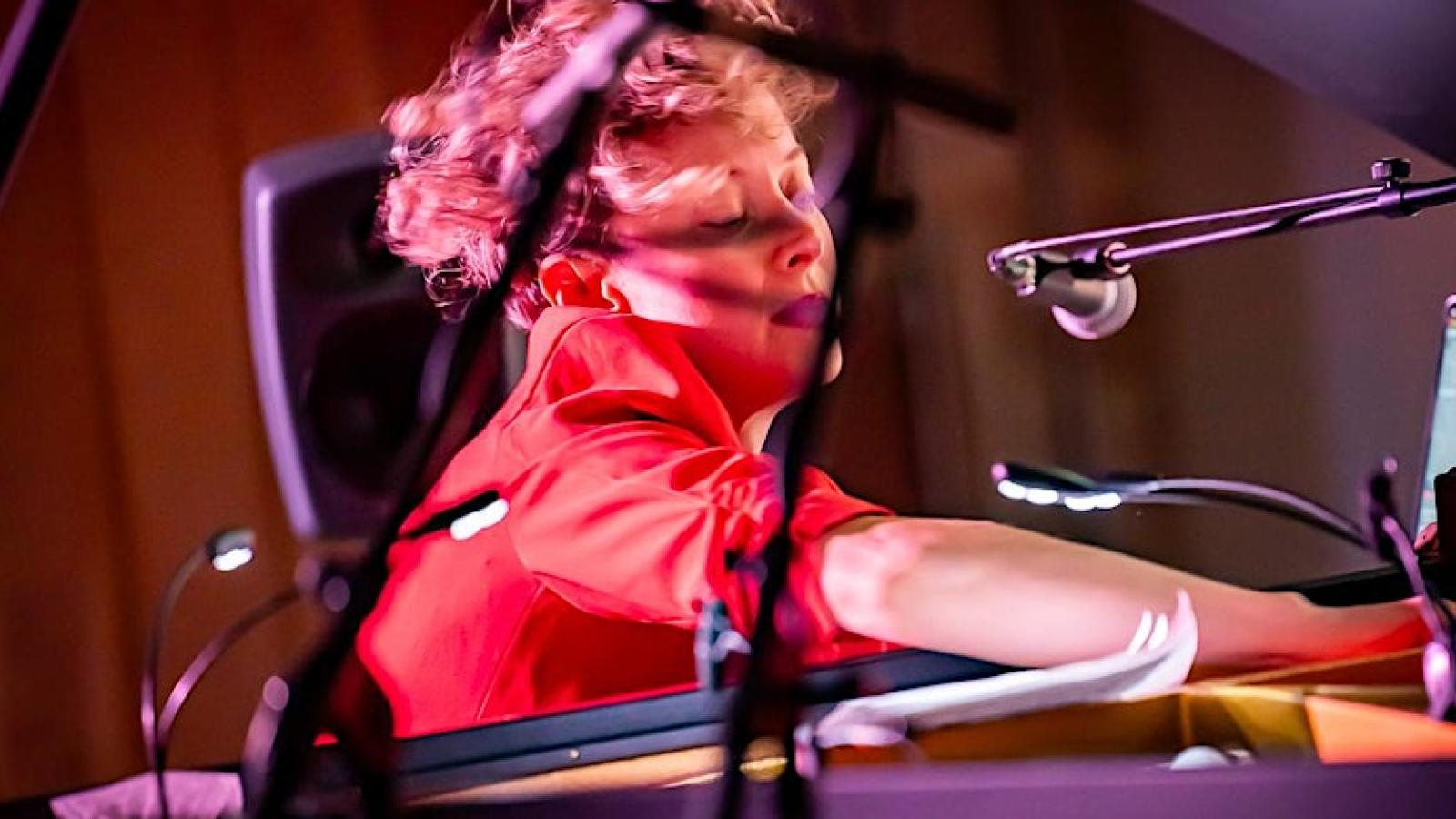 A person with short hair, wearing red, reaching into a piano during a performance at the 2023 Week of Sound.
