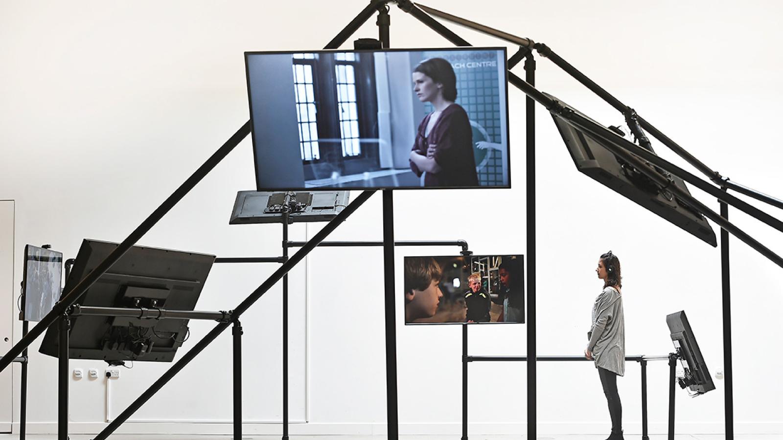 A shot of a person standing under a frame with different sized screens attached to it.