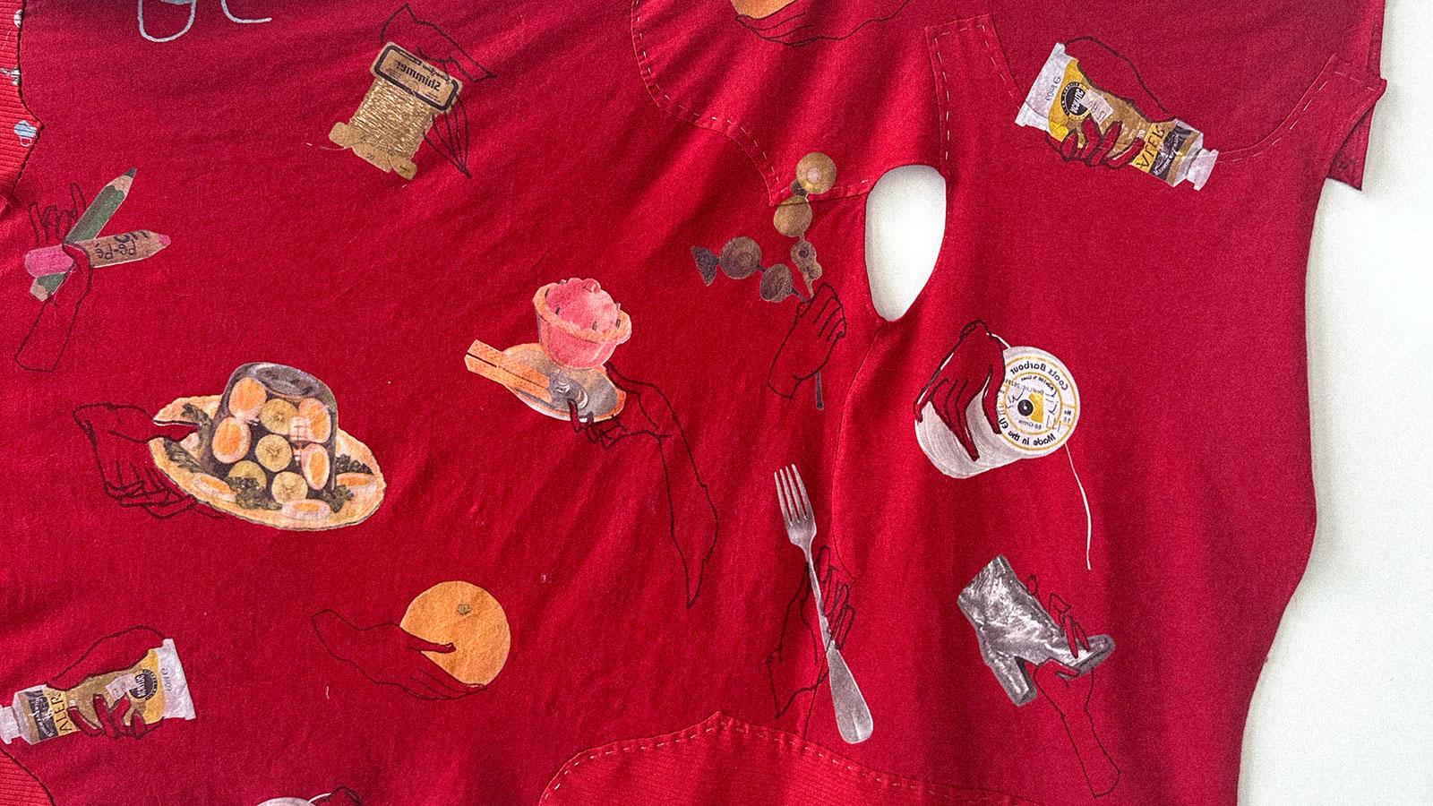 A piece of red material stretched across a wall. It features objects such as hats, boots, cutlery embroidered on it.