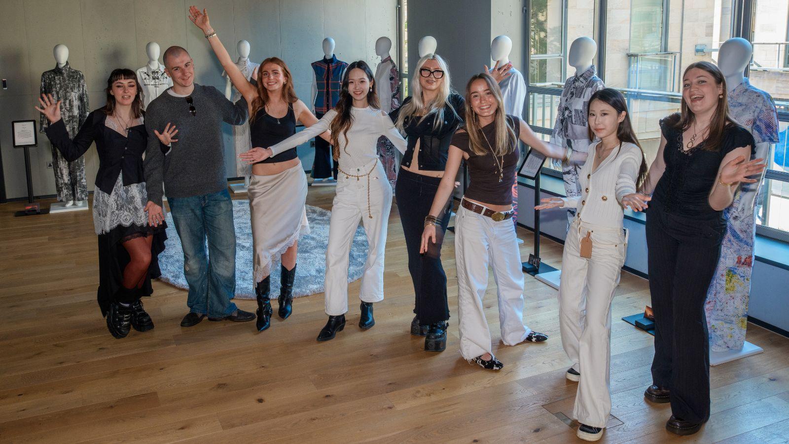 The students stand together in the exhibition room - they're cheering, arms outstretched.