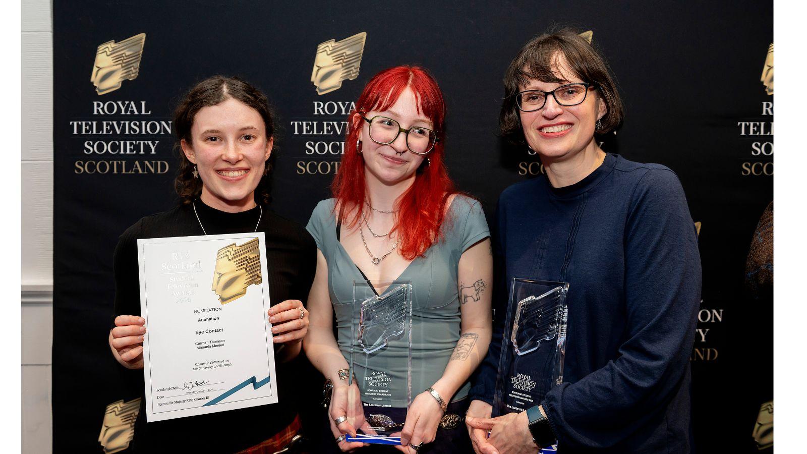 Carmen Thomson, Abby Gilman and Dr Nichola Dobson stand in front of a black board with a logo repeated across it – a gold shape like an angular, abstracted face in profile, and the words Royal Television Society Scotland.