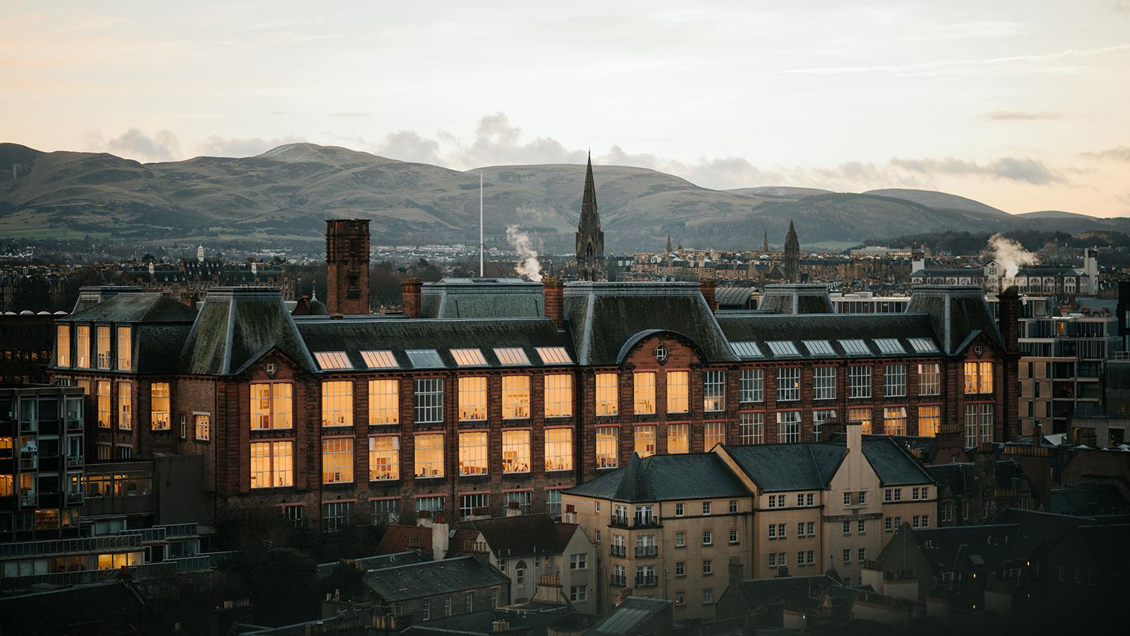 A view of ECA's Main Building on Lauriston Place, with the many large studios lit up. The Pentland hills can be seen in the background.