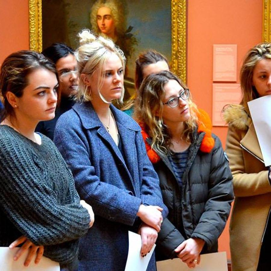 A group of students in a museum being led by a member of staff who is discussing some of the work