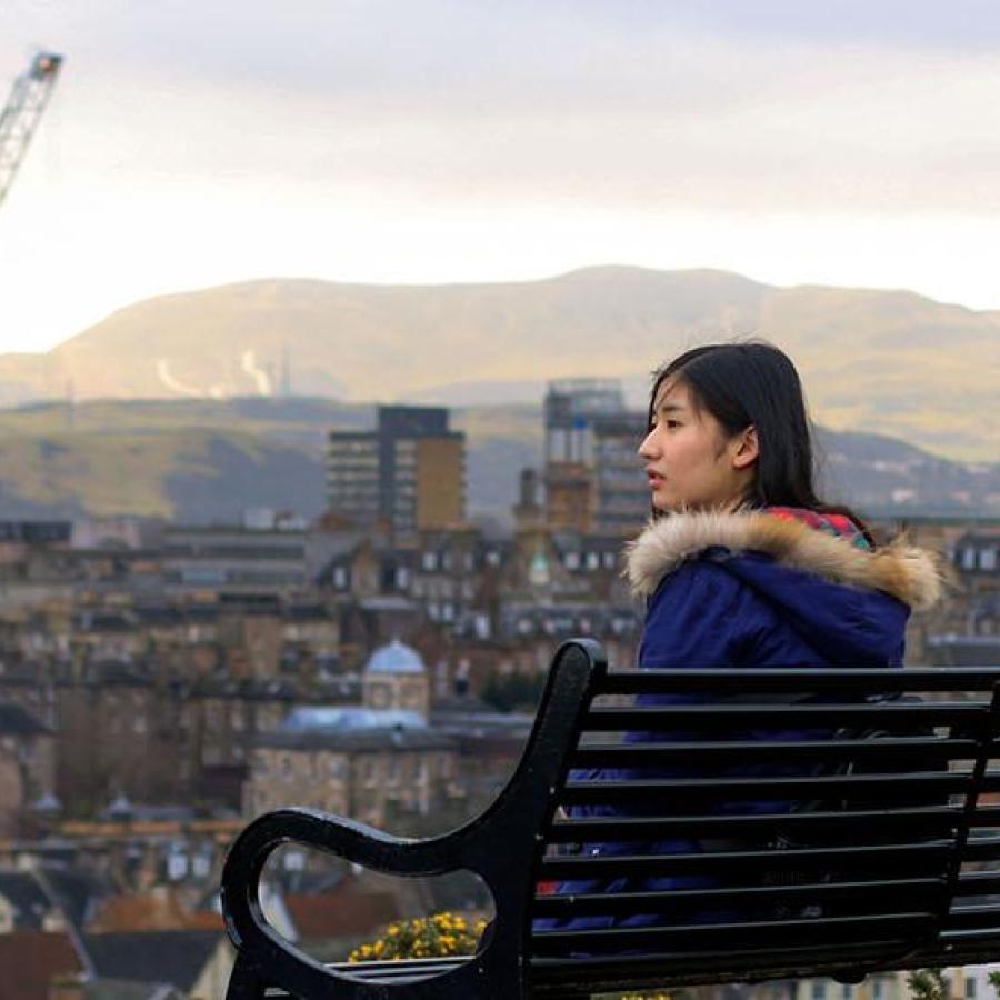A student on a bench looking out over a cityscape of Edinburgh