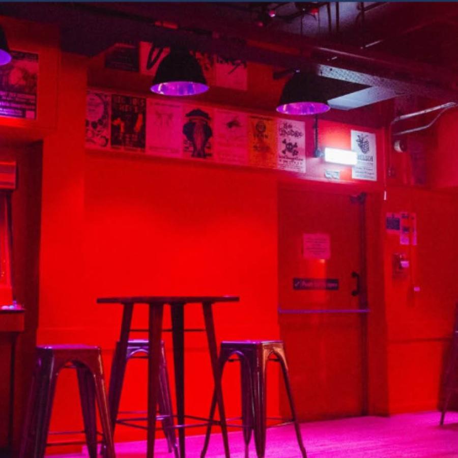 Inside of the Wee Red Bar, showing red painted walls, a retro games machine, and bar stools