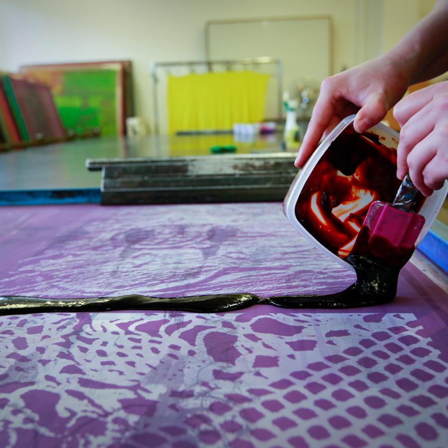 A student pours thick printing ink onto a printing screen.