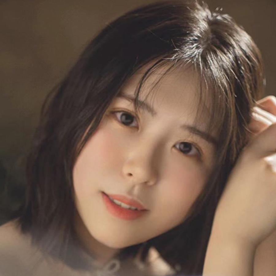 A person with short dark hair, looks directly to the camera and smiles slightly.