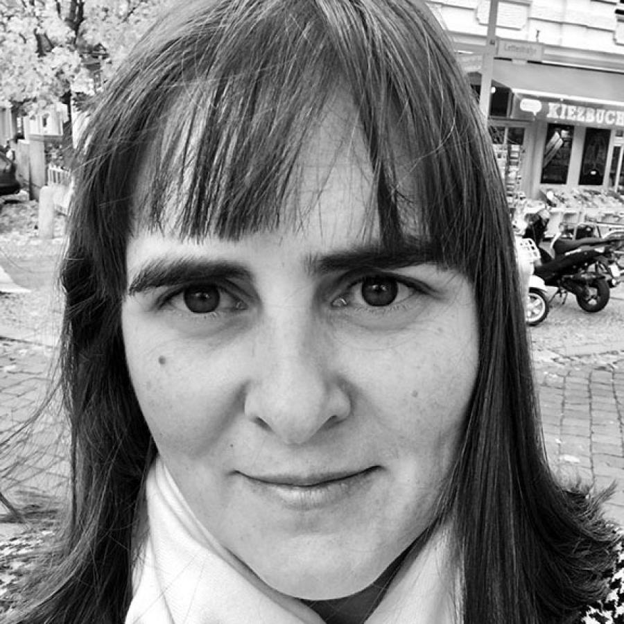 A black and white image of a person with dark hair, wearing a white scarf and looking at the camera.