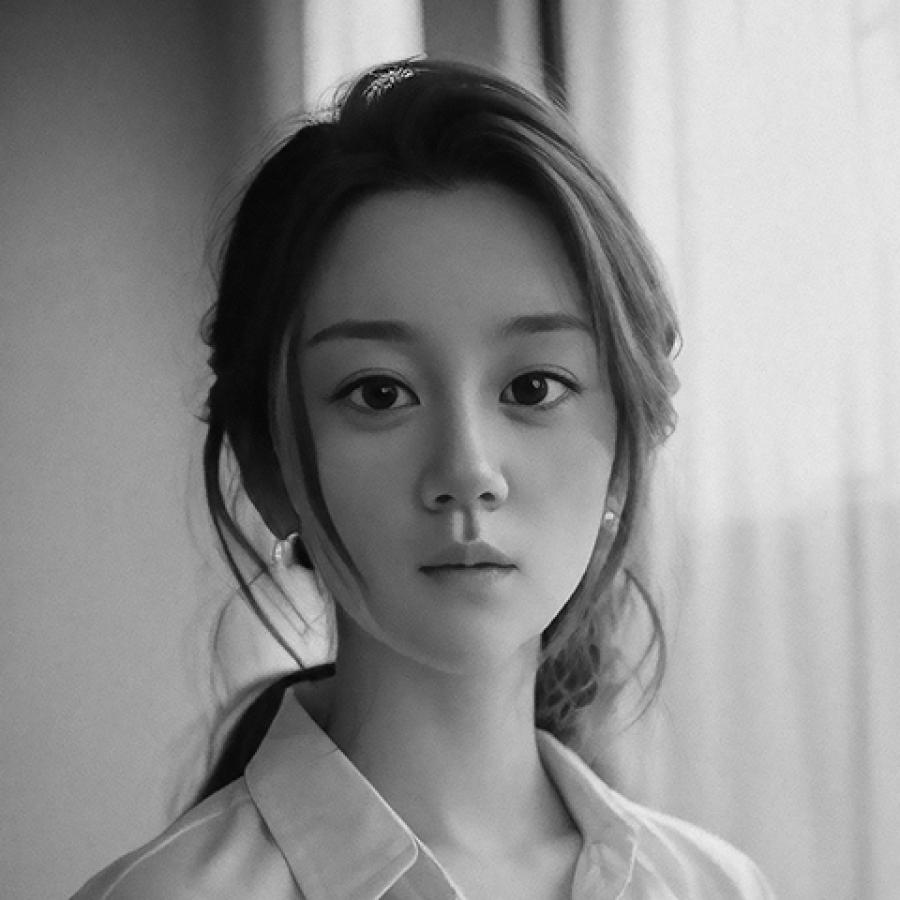 A black and white photo of a person with dark hair tied back, looking to the camera.