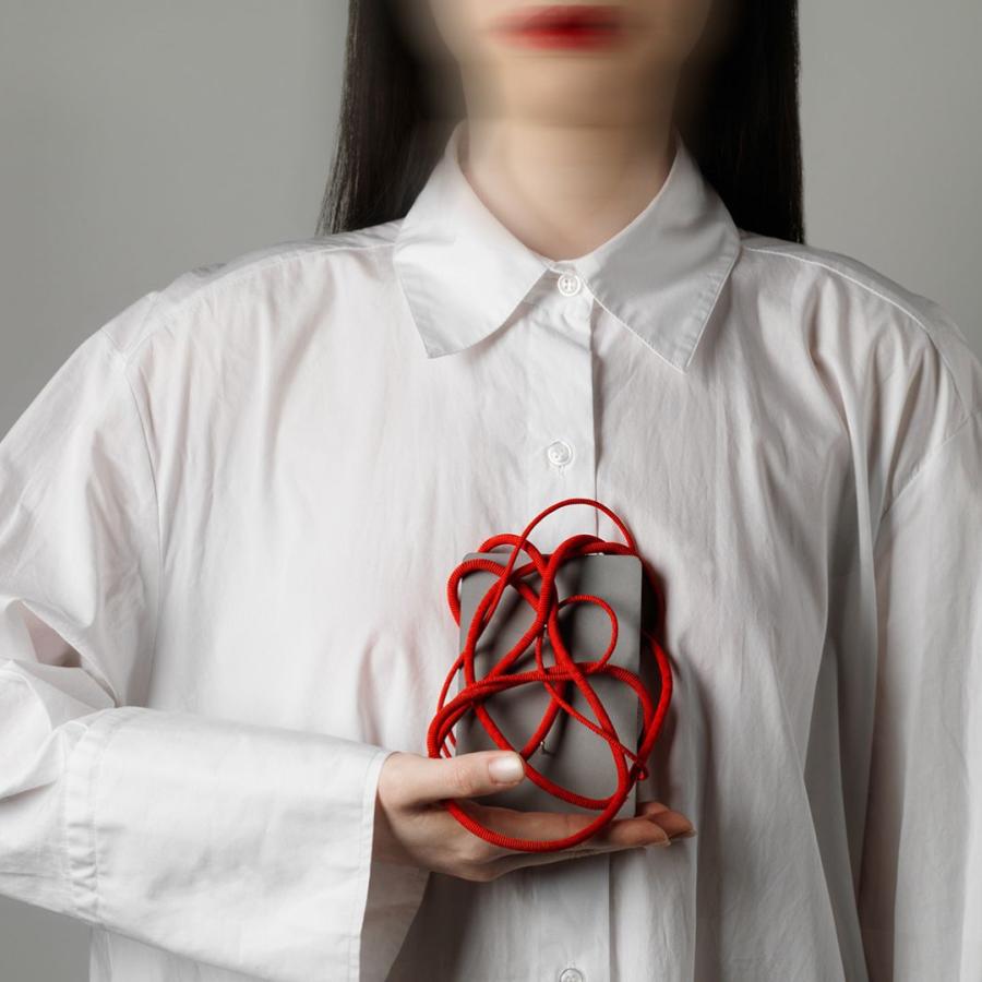 Person wearing a white shirt holds object to chest. The object is a grey box wrapped in a tangle of red cord. 
