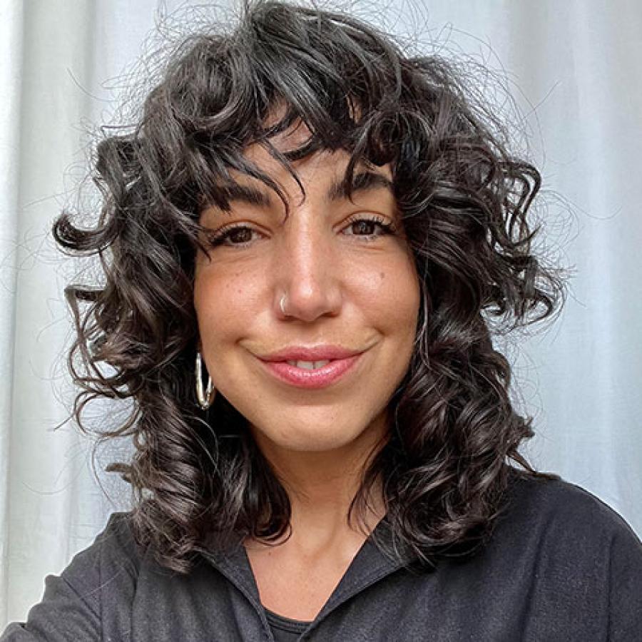 A person with dark curly hair, wearing a black shirt and smiling at the camera.