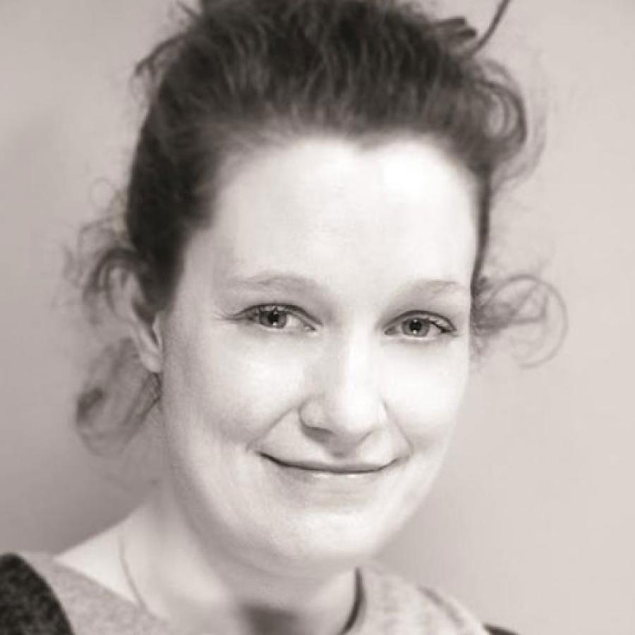 A sepia toned image of a person with their hair tied back, smiling at the camera.