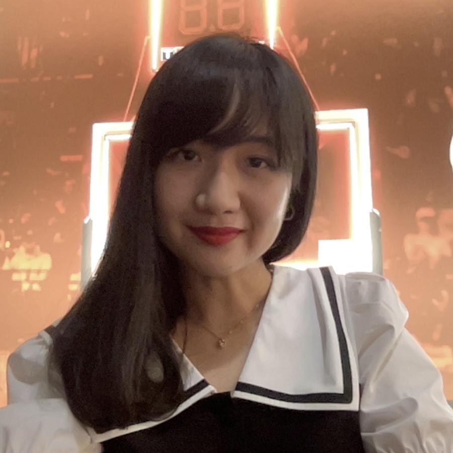 A person with should length dark hair, wearing a white and black blouse with a sailor style collar. They are smiling at the camera.