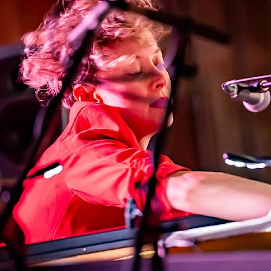 A person with short hair, wearing red, reaching into a piano during a performance at the 2023 Week of Sound.