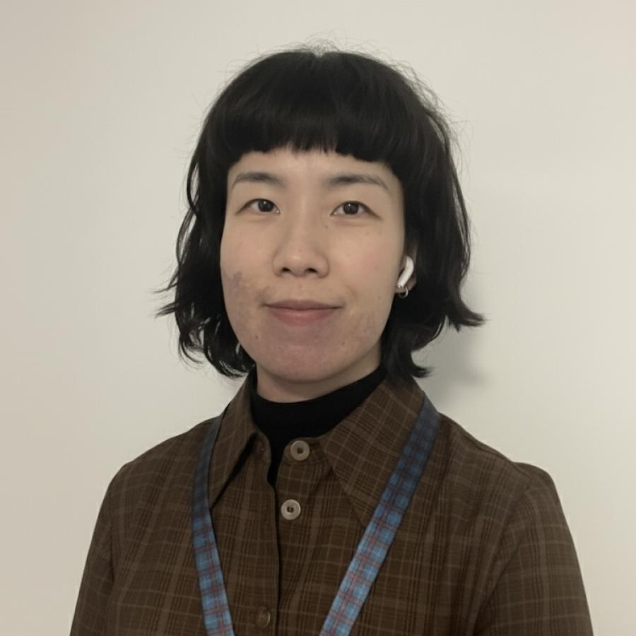 A person with short, dark hair, wearing a brown checked shirt and smiling to the camera.
