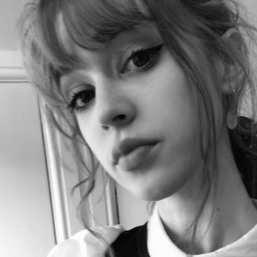 A black and white image of a person with a fringe, black winged eyeliner. They're looking down at the camera.