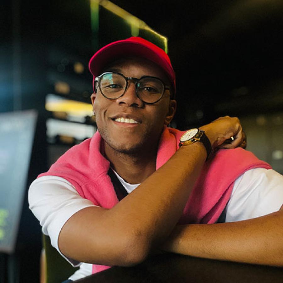 A person wearing a salmon pink vest, white tshirt and hat. They're smiling to the camera.