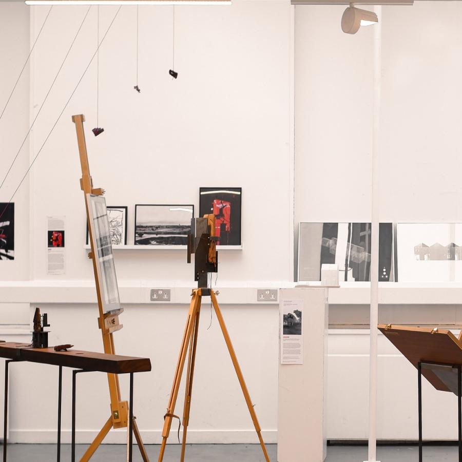 A student reading material in an exhibition, containing models, installations, drawings and photographic prints.