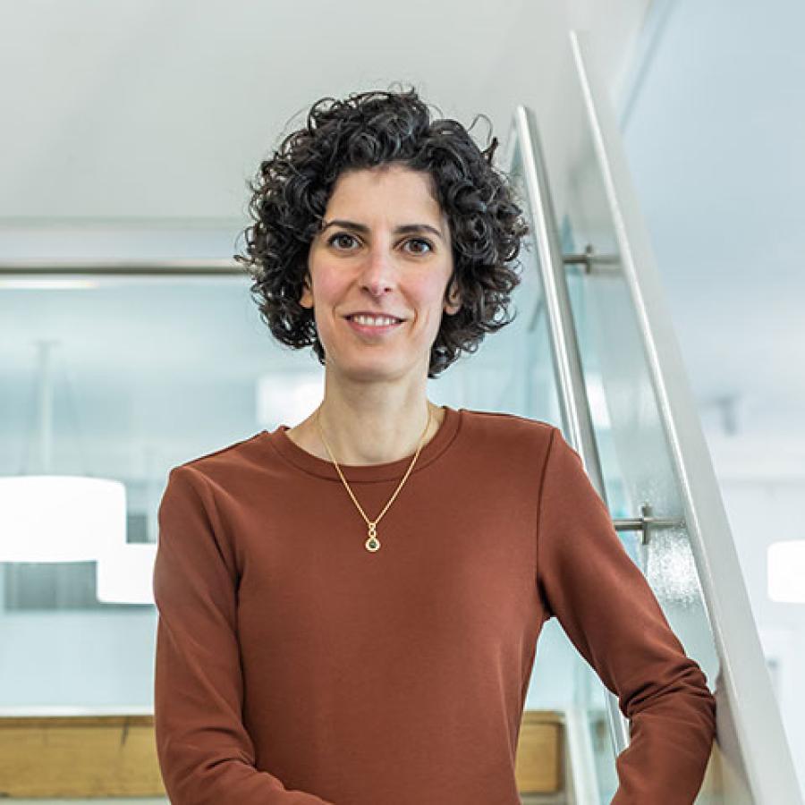 Caterina standing on a set of stairs, wearing an orange/brown coloured dress. They are smiling at the the camera.