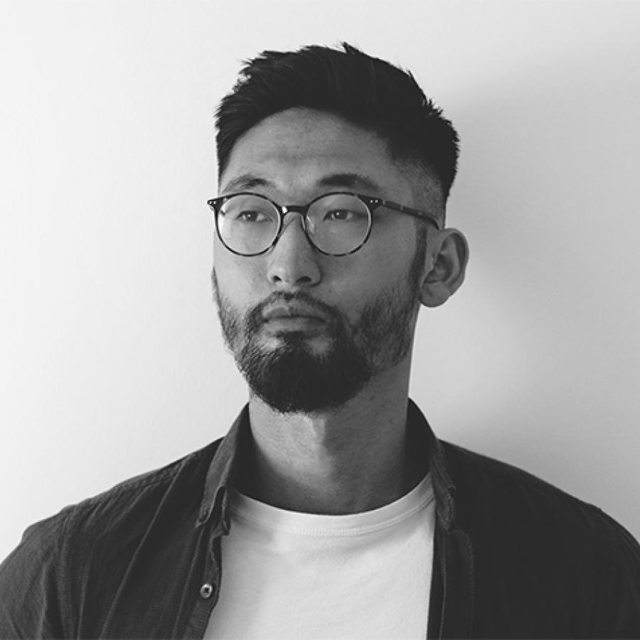 A black and white photo of Thorranze, wearing a white tshirt and dark shirt, glasses, and looking just off camera.