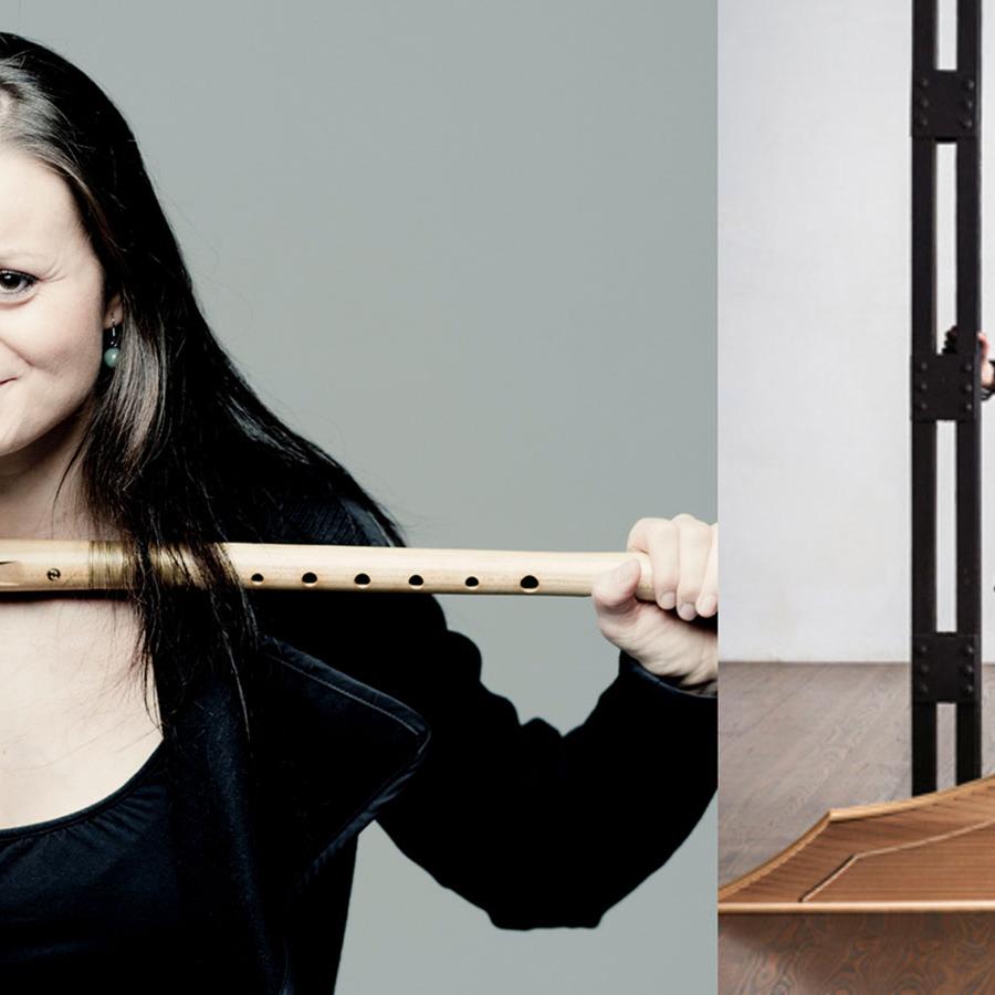Two musicians, one holds their recorder and smiles to the camera, the other walks to a harpsichord that's lying on its side.