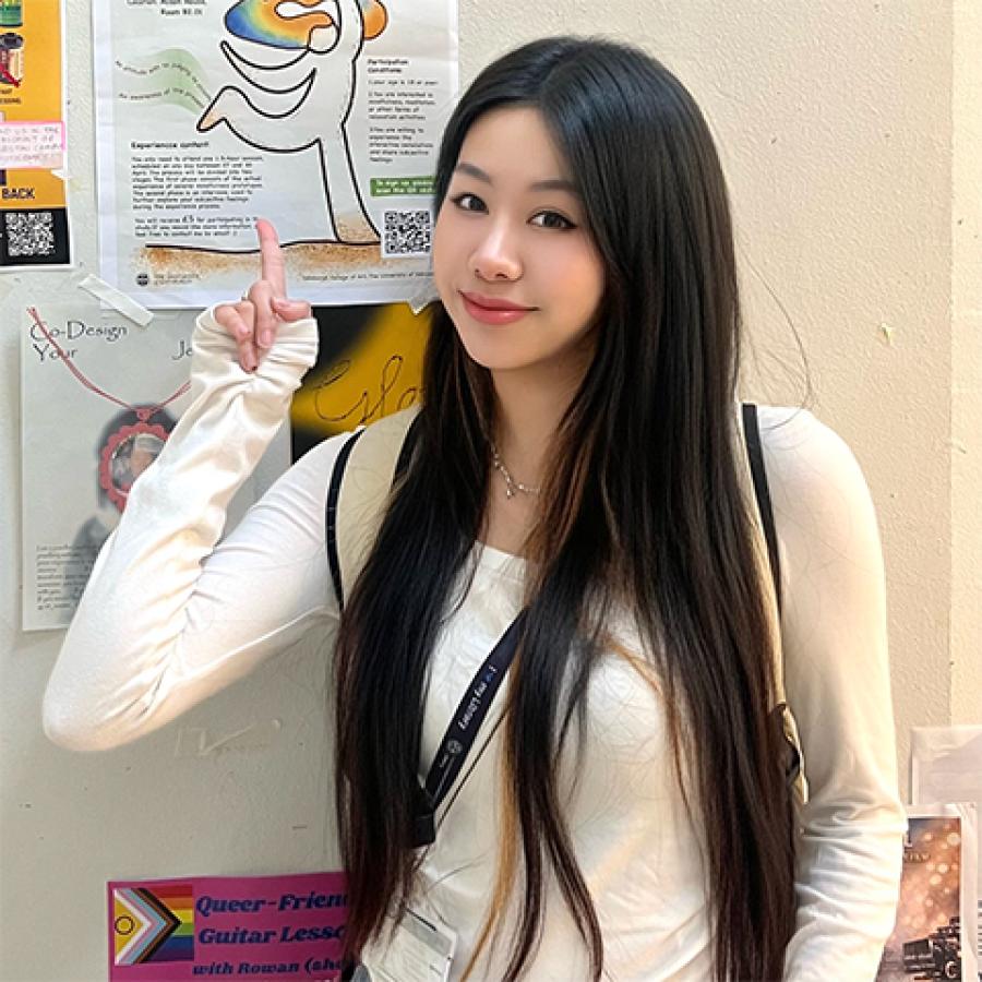 Xiaozhuang Gao stands by a notice board, pointing to a poster.
