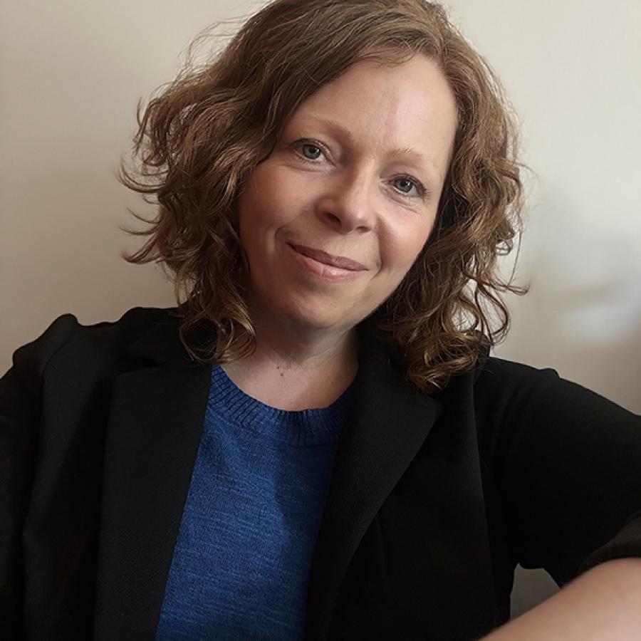A person with short, curly, light brown hair, smiles to the camera.
